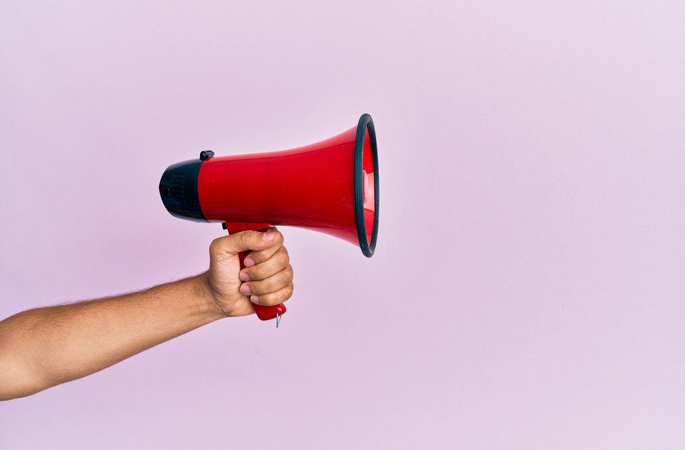 hand of a man holding a red megaphone over isolated pink background