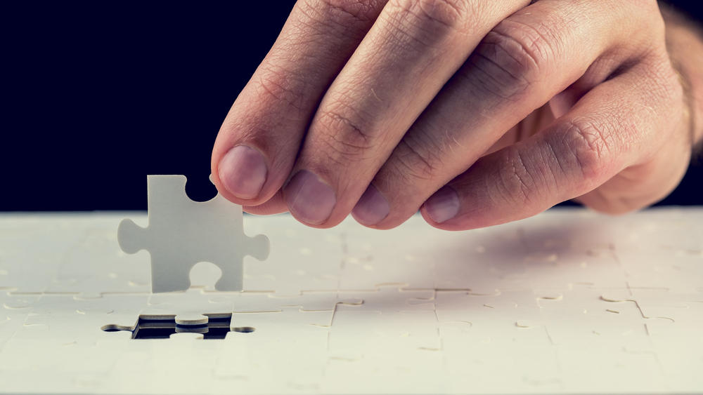 Close up of the hand of a man placing the last piece in place in a jigsaw