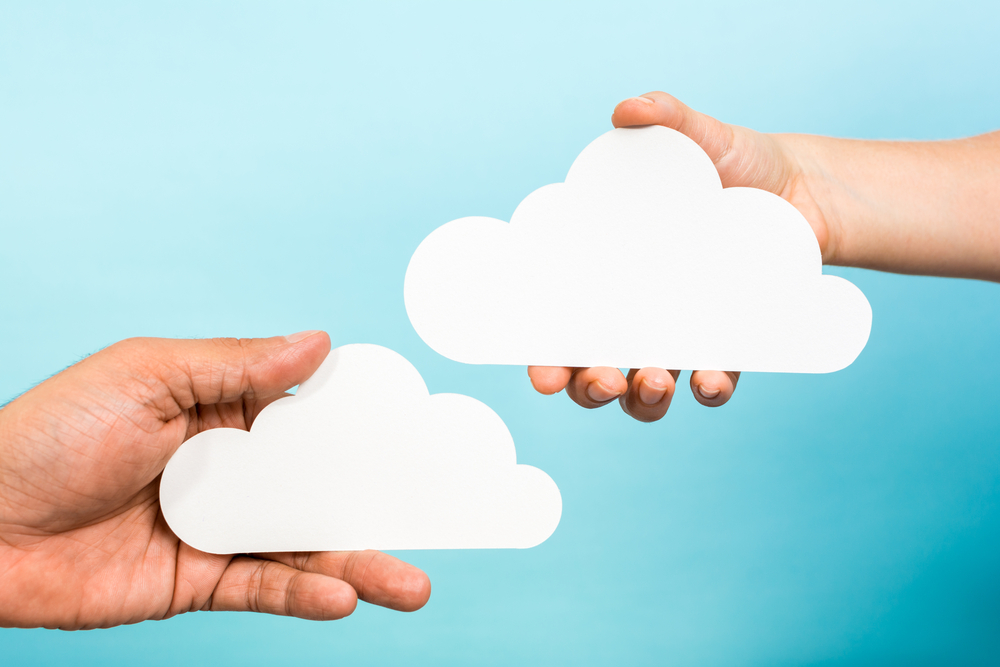 Two hands holding paper clouds on blue background. Cloud computing concept.