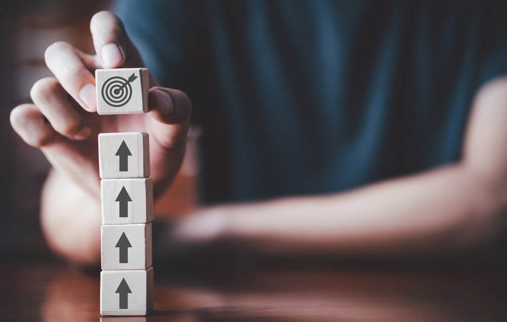 a man holding wooden cube with target board and  placing it on top of arrow icon on wooden table