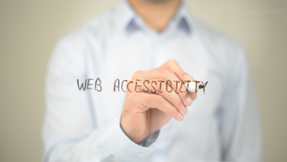 a man writing web accessibility using black marker on transparent board