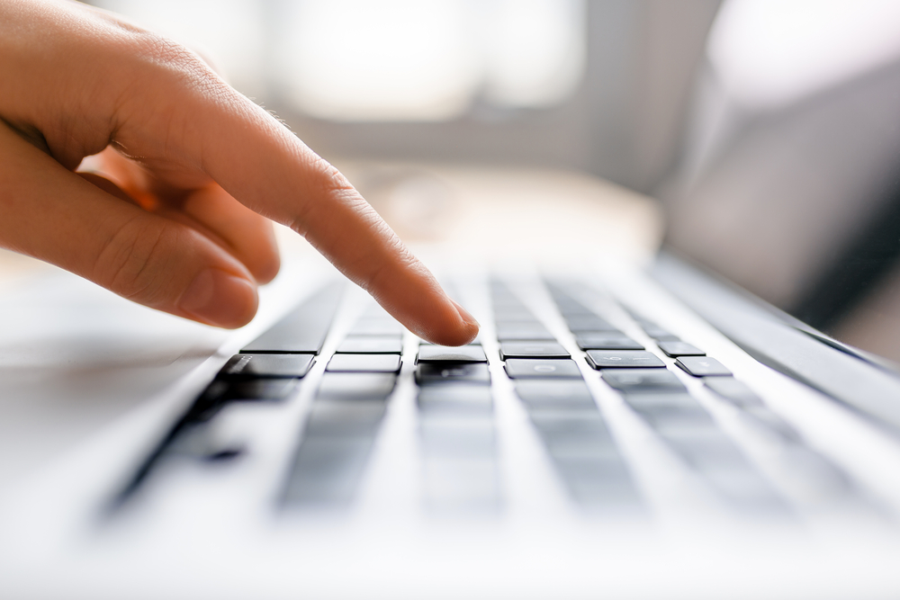 female index finger is about to press a key on laptop keyboard