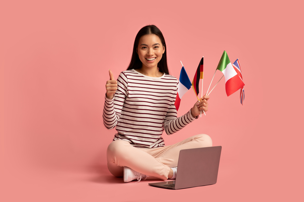woman sitting on floor with laptop and holding different country flags