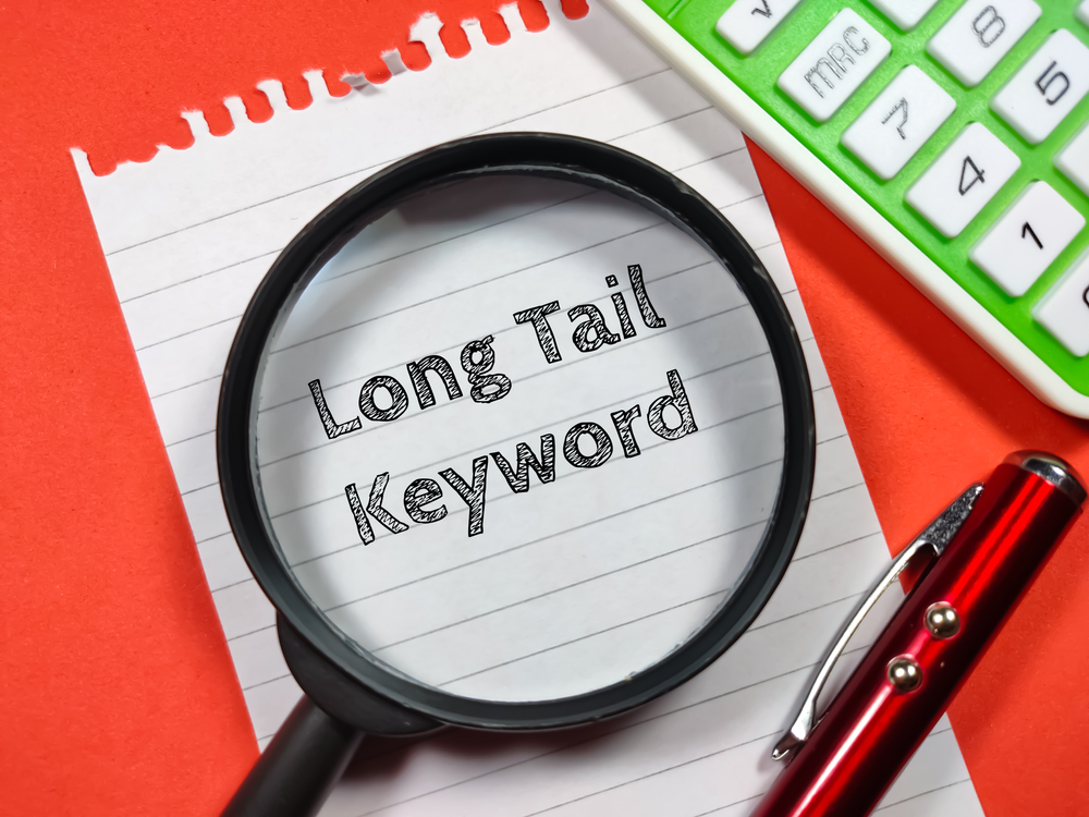 Long Tail Keyword writing on notepaper with magnifying glass,calculator and pen on a red background
