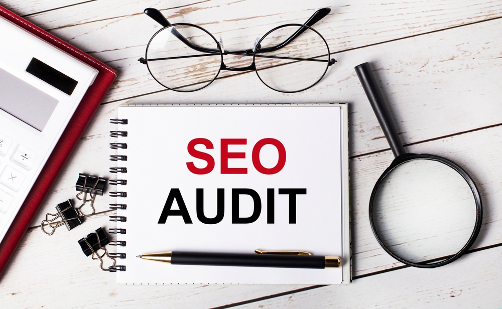 SEO Audit written on white note besides a calculator, plant, and clips on table