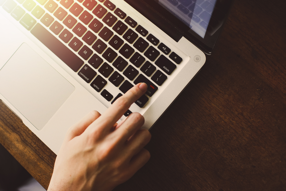 top view of index finger pressing Enter key on laptop keyboard 