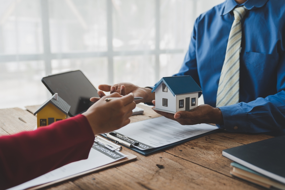 real estate agent holding a small house model and explaining to a client